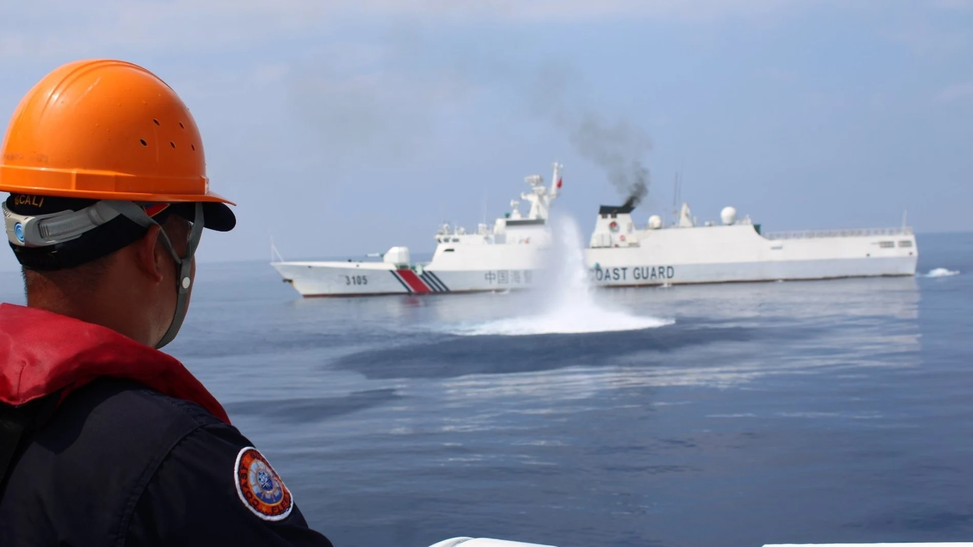 A Filipino coastguard personnel on a patrol vessel viewing a Chinese Coast Guard (CCG) ship firing a water cannon at the vicinity of Scarborough Shoal in the disputed South China Sea