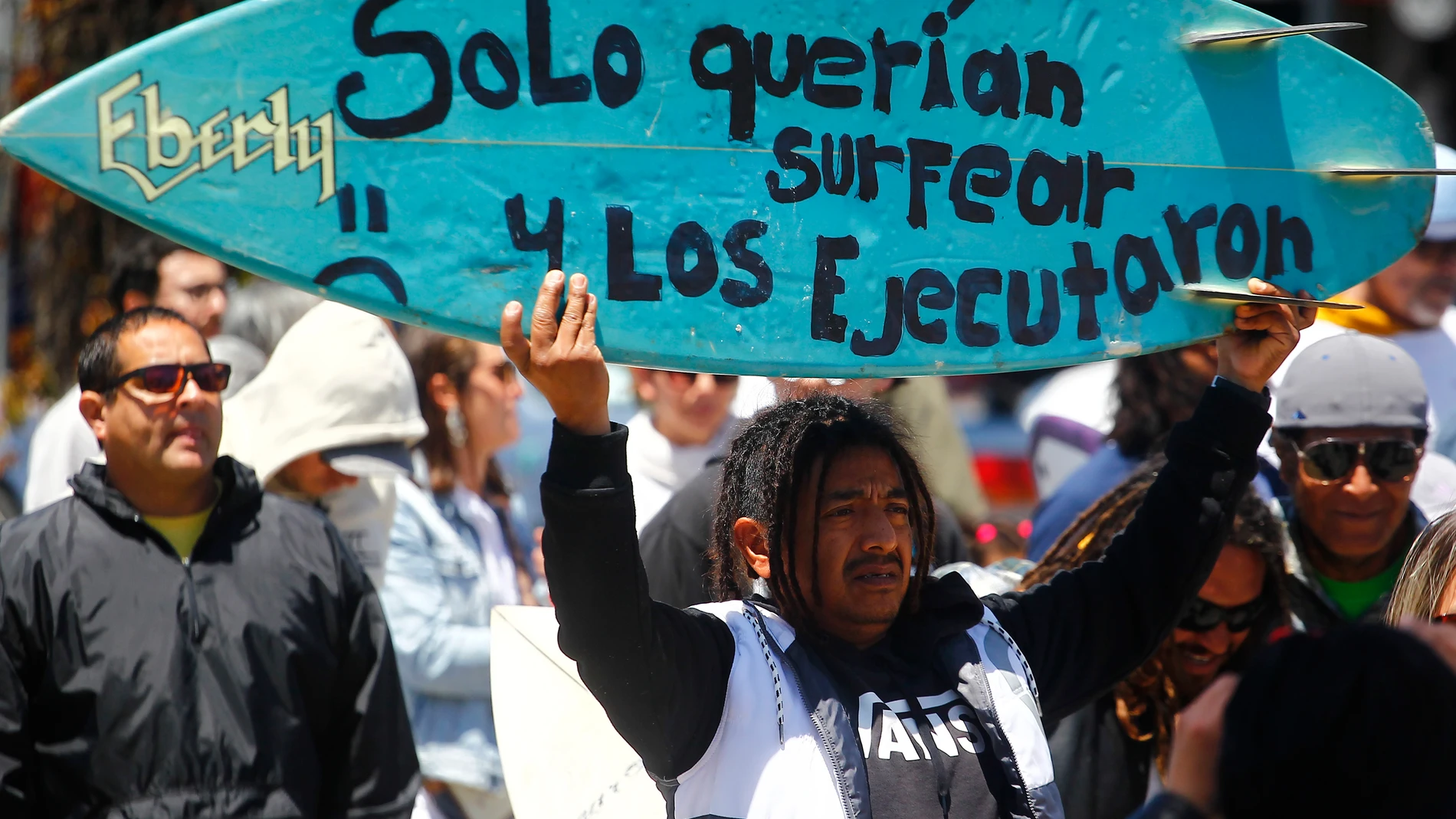 MEX6784. ENSENADA (MÉXICO), 05/05/2024.- Un hombre sostiene una tabla de surf durante una manifestación para exigir justicia por el asesinato de tres surfistas extranjeros este domingo, en la ciudad de Ensenada (México). Autoridades mexicanas señalaron este domingo que el probable homicidio de los tres surfistas extranjeros cerca de Ensenada (Baja California), en el noroeste de México, fue por el robo de un vehículo en el que viajaban y que los cuerpos presentan "orificio por arma de fuego en...