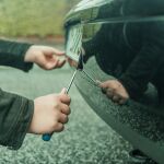 Una persona roba la matrícula de un coche aparcado con un destornillador