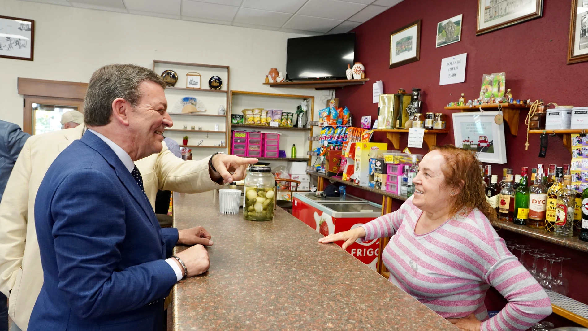 El consejero de la Presidencia, Luis Miguel González Gago, conversa con la mujer que regenta el bar de la Santa Espina, antes de explicar la línea de ayudas