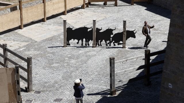 GRAFCAV3666. PAMPLONA, 13/06/2024.- Un turista se fotografía junto al perfil de 5 toros a escala real sobre chapa metálica colocados en los corrales de la Cuesta de Santo Domingo. La instalación se ubica aproximadamente en el centro de la plaza. De izquierda a derecha, los animales pasan de una actitud más estática a otra activa y dinámica simulando la situación en el momento del lanzamiento del cohete que da comienzo al encierro diario. EFE/ Jesús Diges