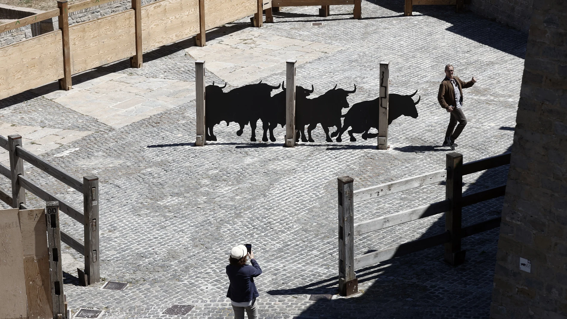 GRAFCAV3666. PAMPLONA, 13/06/2024.- Un turista se fotografía junto al perfil de 5 toros a escala real sobre chapa metálica colocados en los corrales de la Cuesta de Santo Domingo. La instalación se ubica aproximadamente en el centro de la plaza. De izquierda a derecha, los animales pasan de una actitud más estática a otra activa y dinámica simulando la situación en el momento del lanzamiento del cohete que da comienzo al encierro diario. EFE/ Jesús Diges