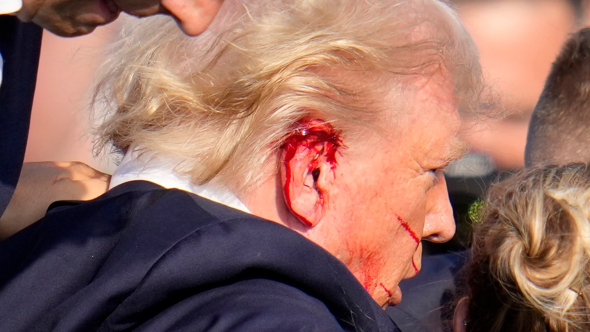Republican candidate Donald Trump is seen with what appears to be blood on his face surrounded by secret service agents as he is taken off the stage at a campaign event at Butler Farm Show Inc. in Butler, Pennsylvania, July 13, 2024. - Republican candidate Donald Trump was evacuated from the stage at today's rally after what sounded like shots rang out at the event in Pennsylvania, according to AFP. The former US president was seen with blood on his right ear as he was surrounded by security