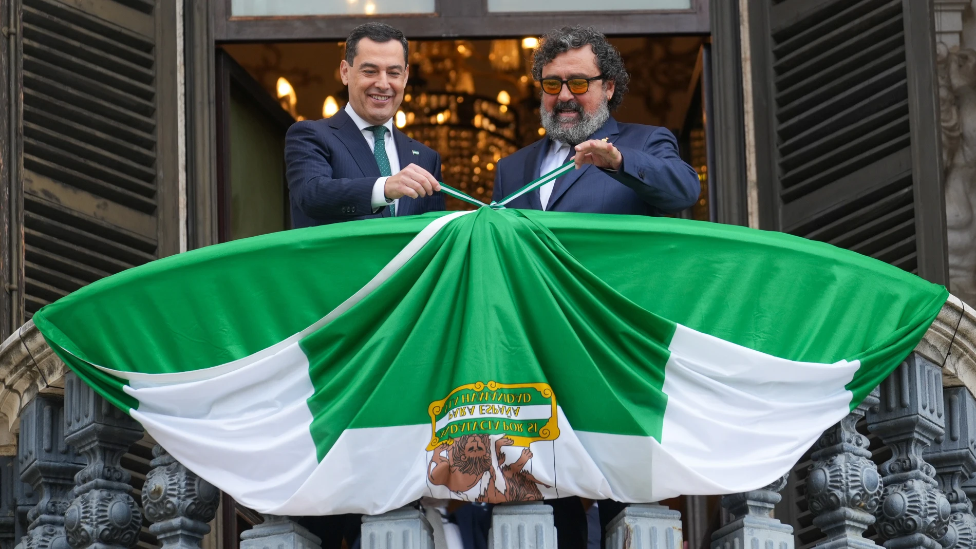 El presidente de la Junta de Andalucía, Juanma Moreno, y el actor Paco Tous despliegan este miércoles la bandera de Andalucía en un balcón del Palacio de San Telmo en Sevilla. FRANCISCO J.OLMO/EUROPA PRESS 04/12/2024