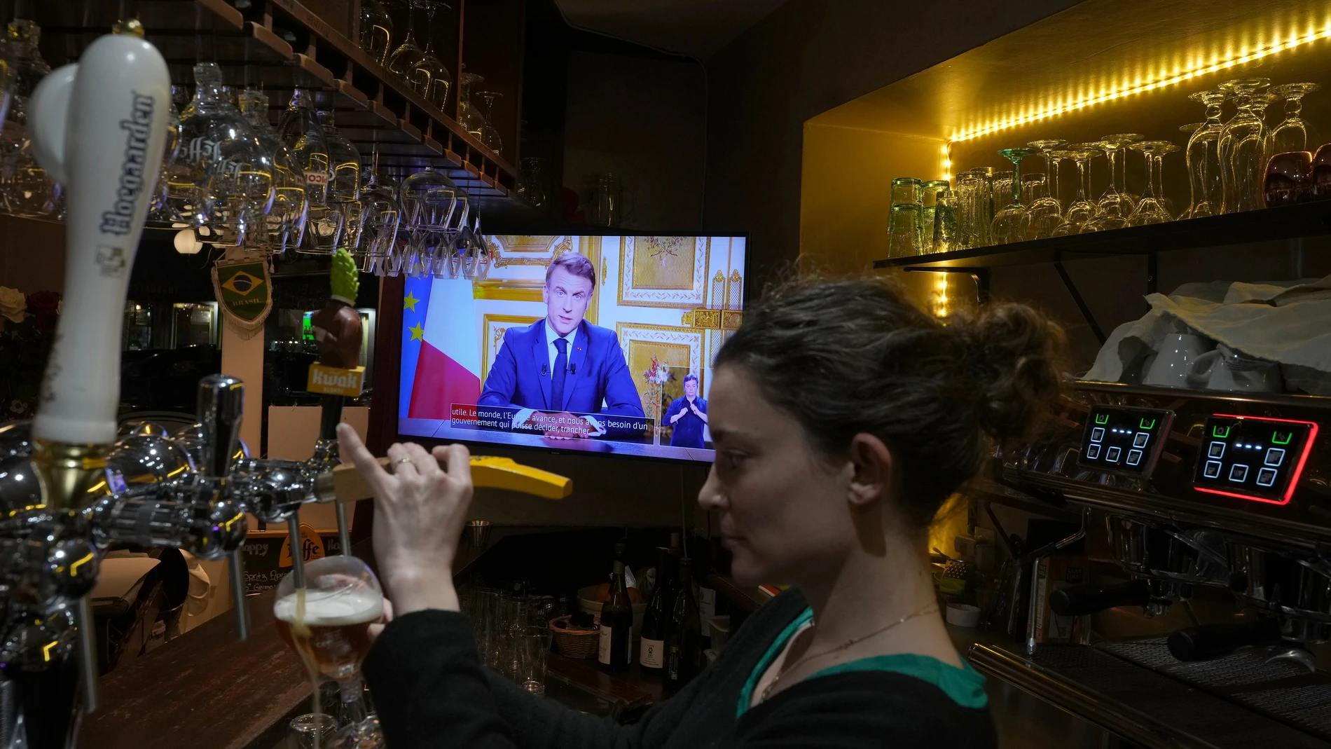 A waiter serves a beer as French President Emmanuel Macron addresses the nation following the resignation of ousted Prime Minister Michel Barnier, a day after a historic no-confidence vote at the National Assembly left France without a functioning government. Thursday, Dec. 5, 2024 in Versailles, outside Paris. (AP Photo/Michel Euler)