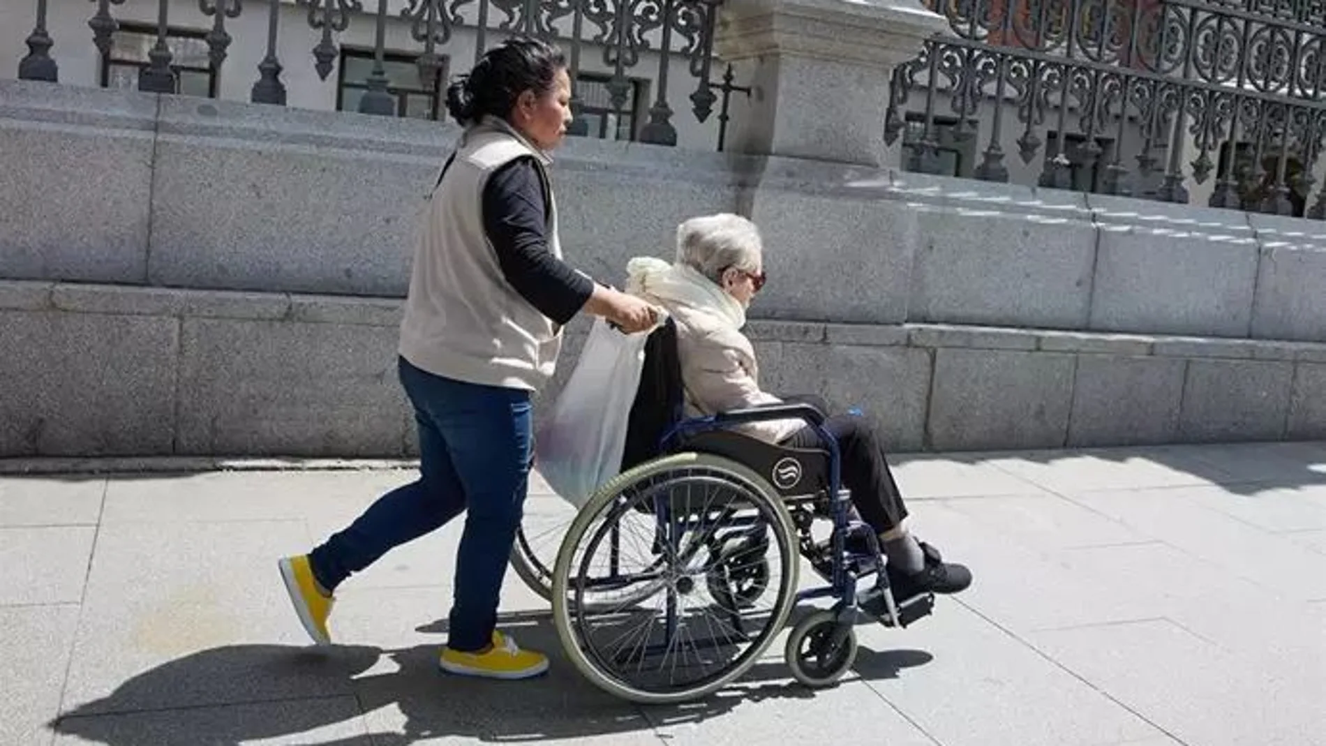 Una mujer mayor en silla de ruedas y su cuidadora pasean por el centro de la ciudad