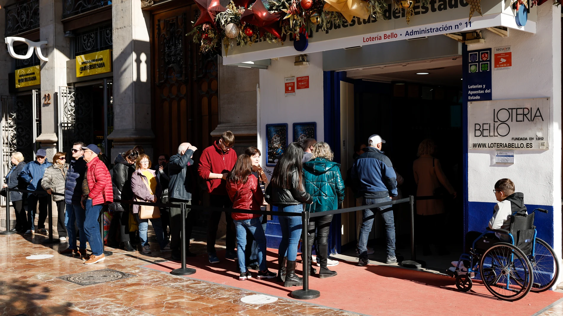 GRAFCVA4485. VALENCIA, 20/12/2024.- Varias personas hacen cola en una administración de lotería durante este viernes cuando las peticiones de lotería del Gordo de Navidad de Valencia desde el resto de España se han disparado este año en las administraciones de la ciudad y de los municipios a consecuencia de la dana, también entre el voluntariado, y al mismo tiempo la catástrofe ha hecho que decaigan las compras de clientes habituales, como empresas o asociaciones de la zona afectada. EFE/Biel...