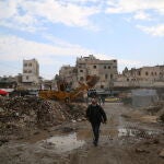 Un hombre camina junto a una excavadora que retira escombros en Alepo (Siria)