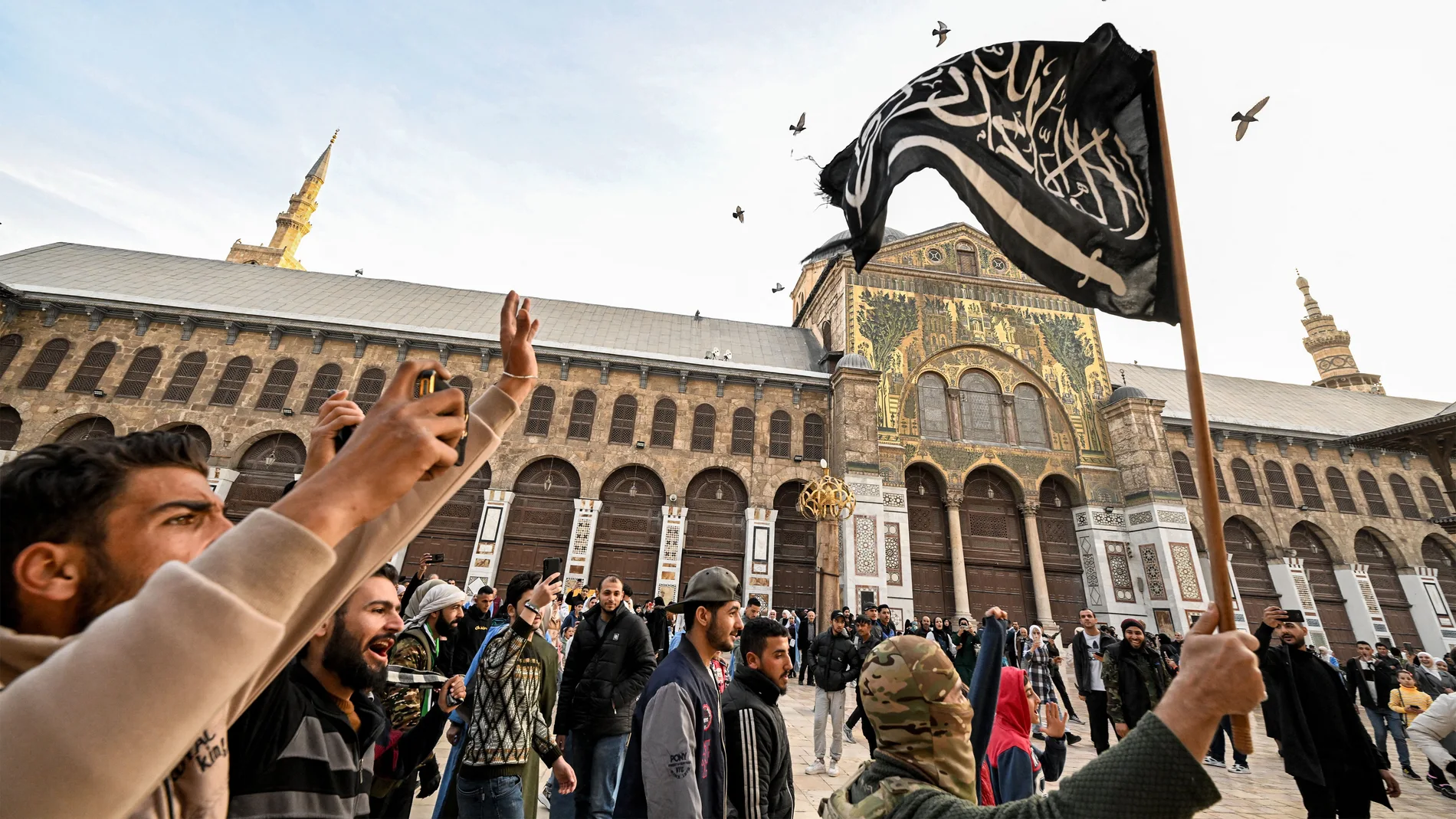 A Syrian rebel fighter holds an Islamist black flag depicting the Islamic Shahada (the creed stating a belief in one god and the acceptance that Mohammed was God's prophet), while walking in the courtyard of the 8th-century Umayyad Mosque in Damascus on December 10, 2024. - Islamist-led rebels took Damascus in a lightning offensive on December 8, ousting president Bashar al-Assad and ending five decades of Baath rule in Syria. (Photo by LOUAI BESHARA / AFP)