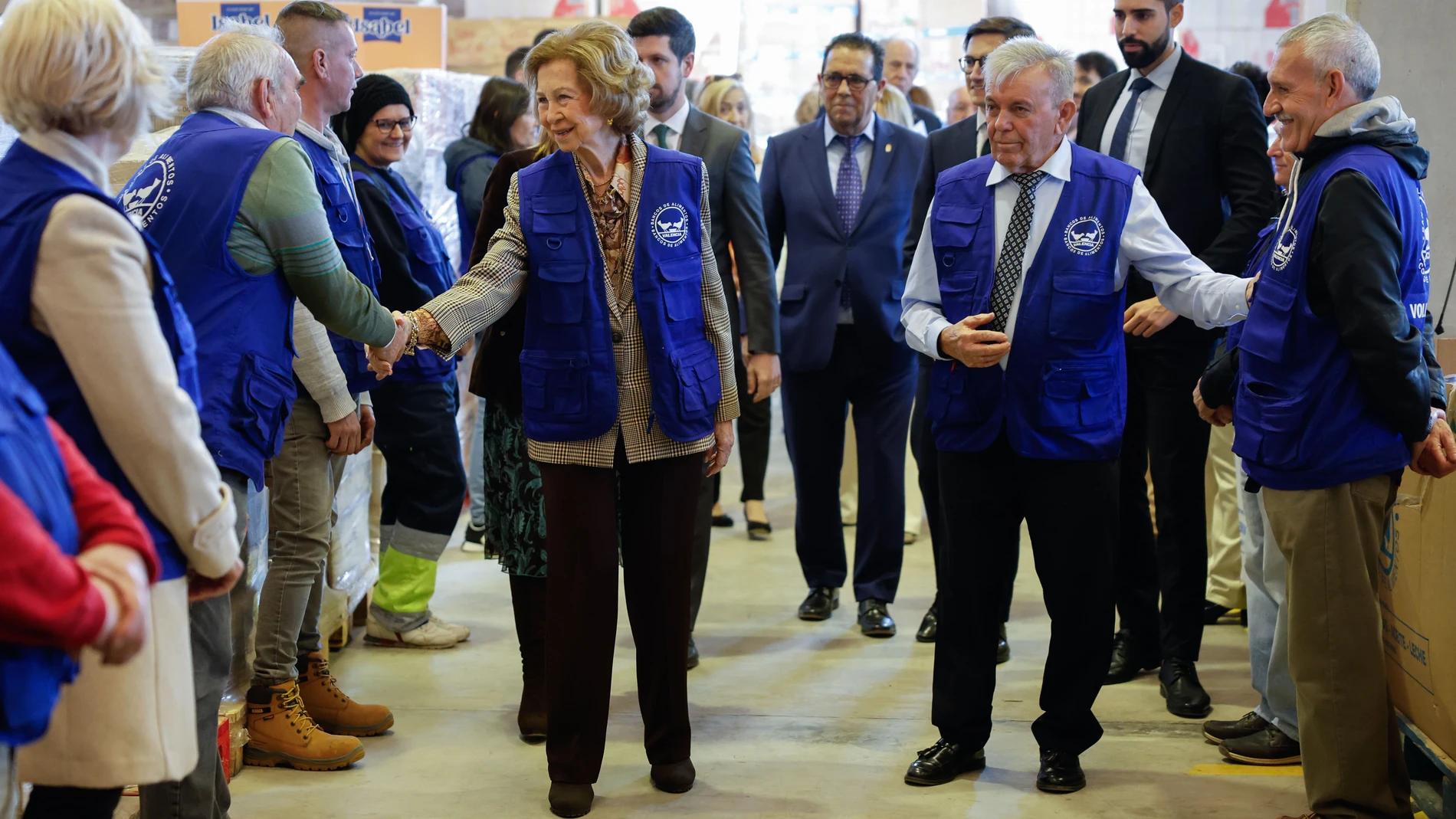 LA POBLA DE VALLBONA (VALENCIA) 28/01/2025.- La reina Sofía (c-i) junto al presidente del Banco de Alimentos de Valencia, Jaime Serra (c-d) saludan a los empleados durante su visita al Banco de Alimentos de Valencia este jueves para conocer su actuación tras la dana del 29 de octubre. EFE/ Ana Escobar
