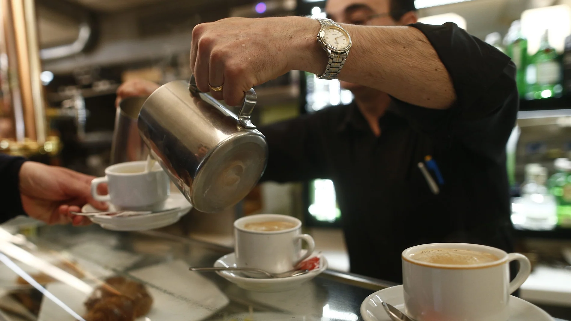 Un camarero sirviendo varios cafés en la barra de un bar