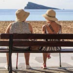 Dos mujeres disfrutan del buen tiempo sentadas ante la playa de Levante de Benidorm