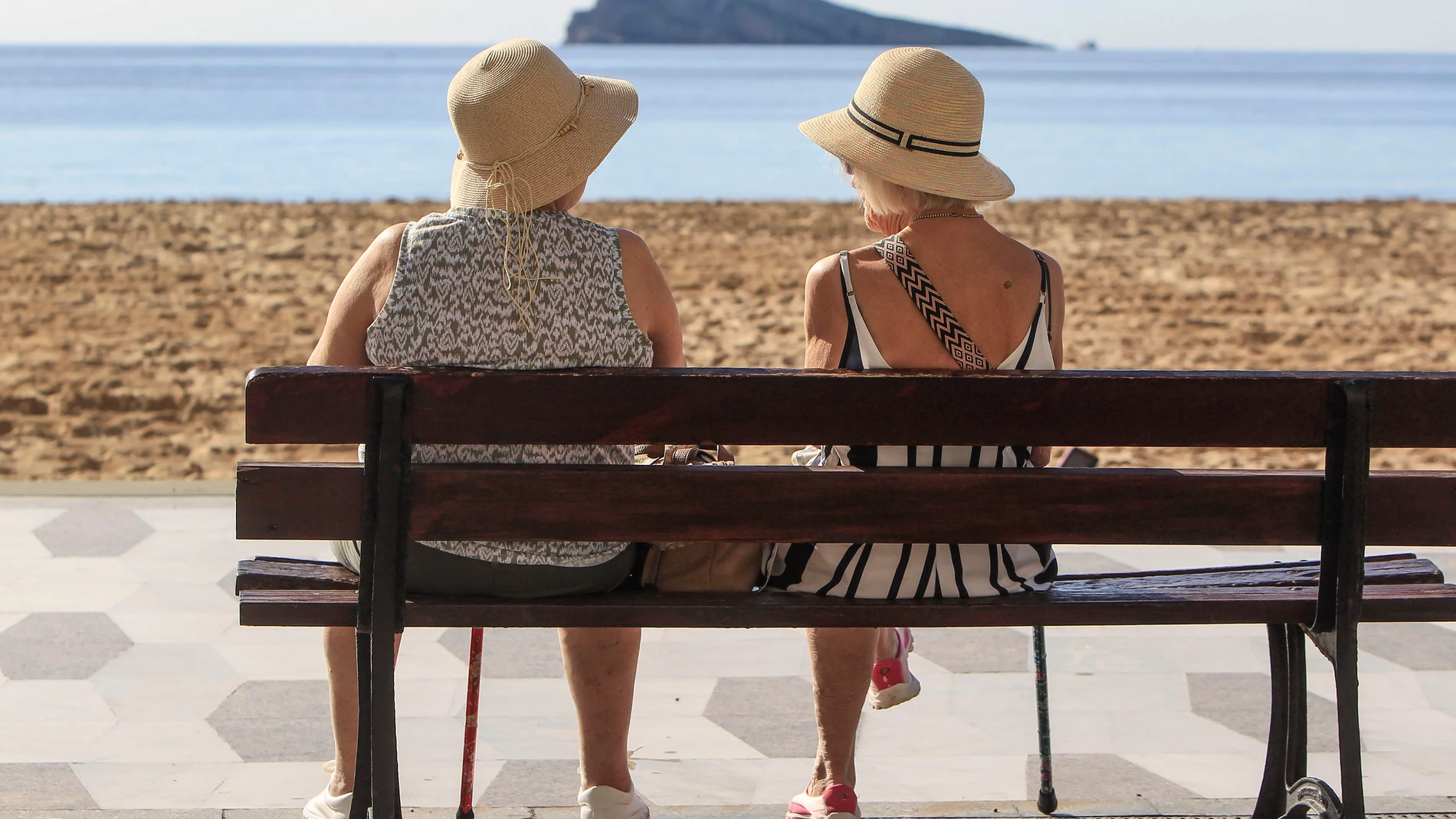 Dos mujeres disfrutan del buen tiempo sentadas ante la playa de Levante de Benidorm