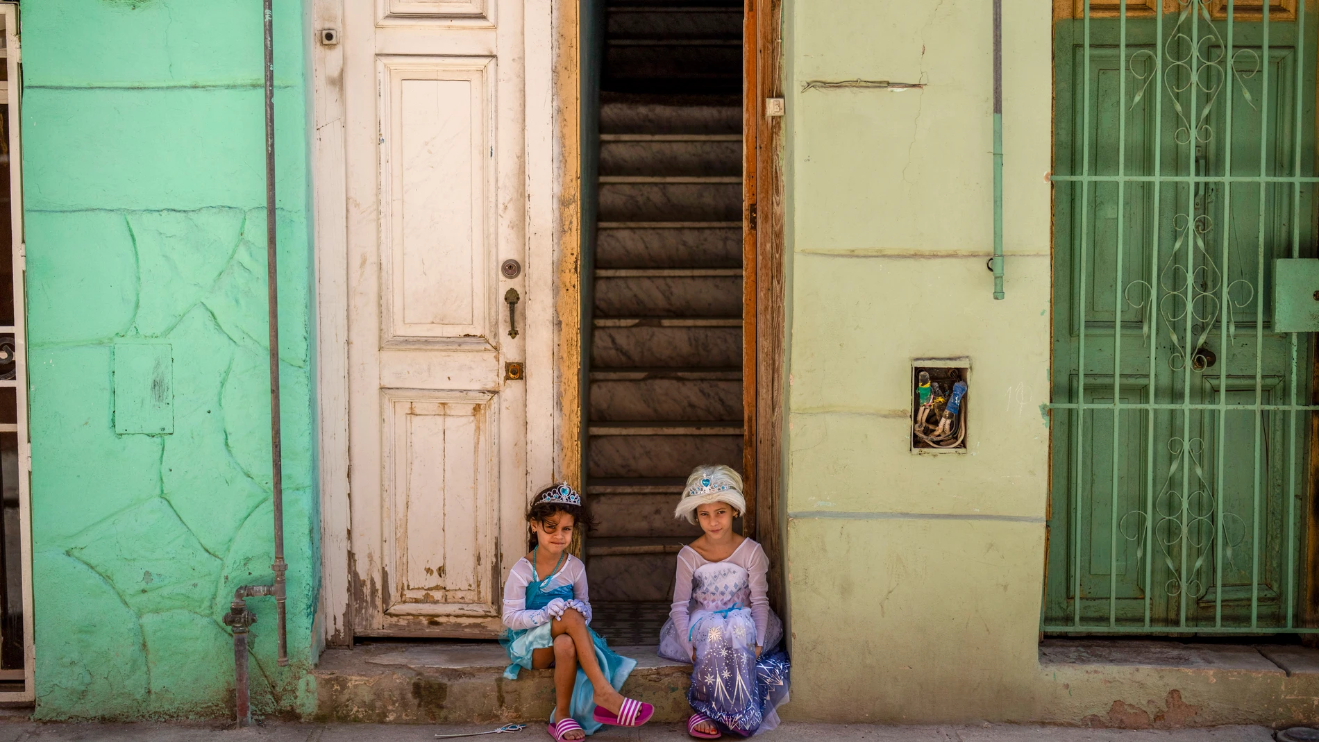 Girls playing dress up sit in the doorway of a home in Havana, Cuba, Friday, Feb. 14, 2025. (AP Photo/Ramon Espinosa)