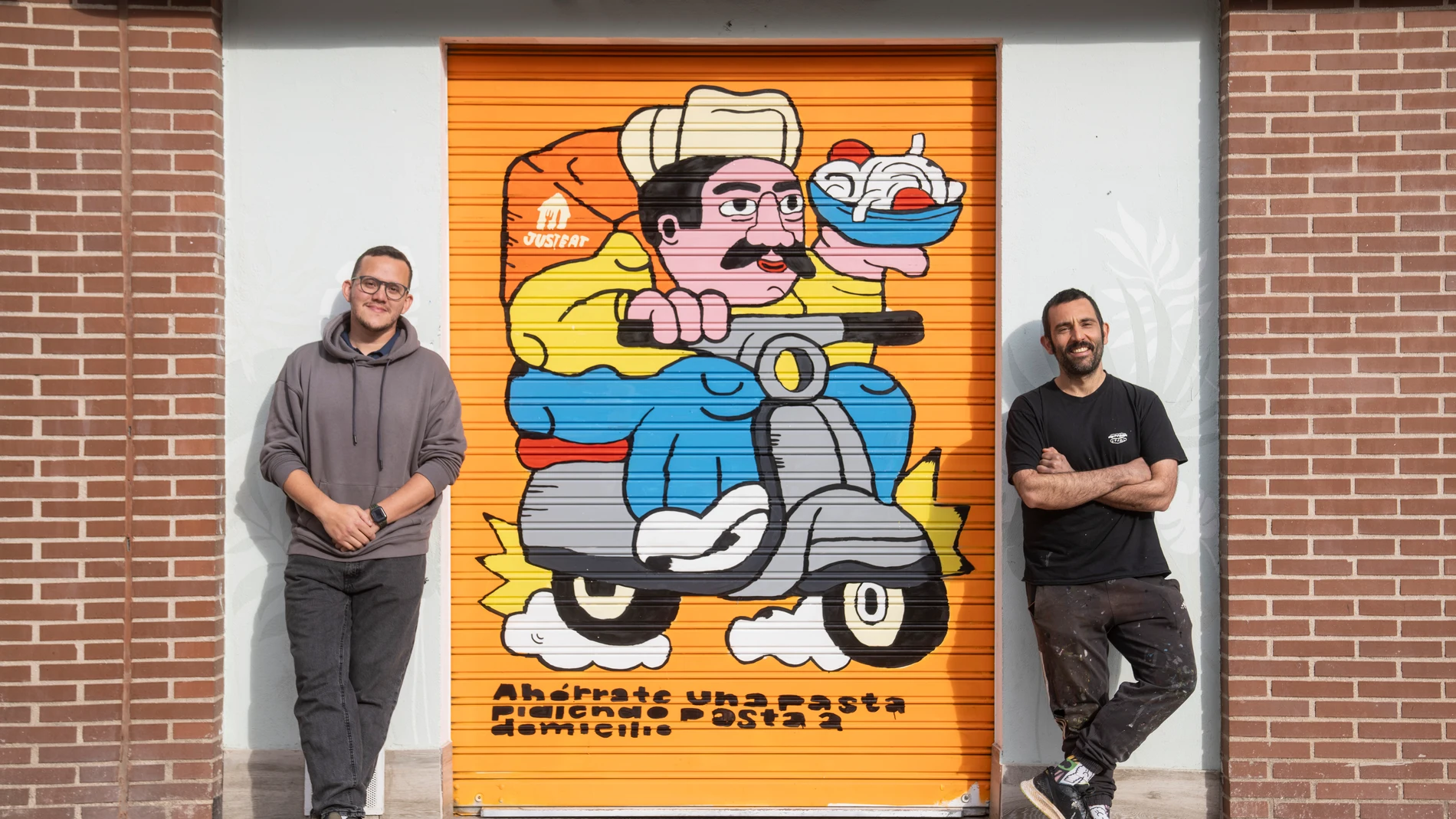 Propietario de L'Artigiano junto al artista que ha pintado su cierre en una campaña de Just Eat