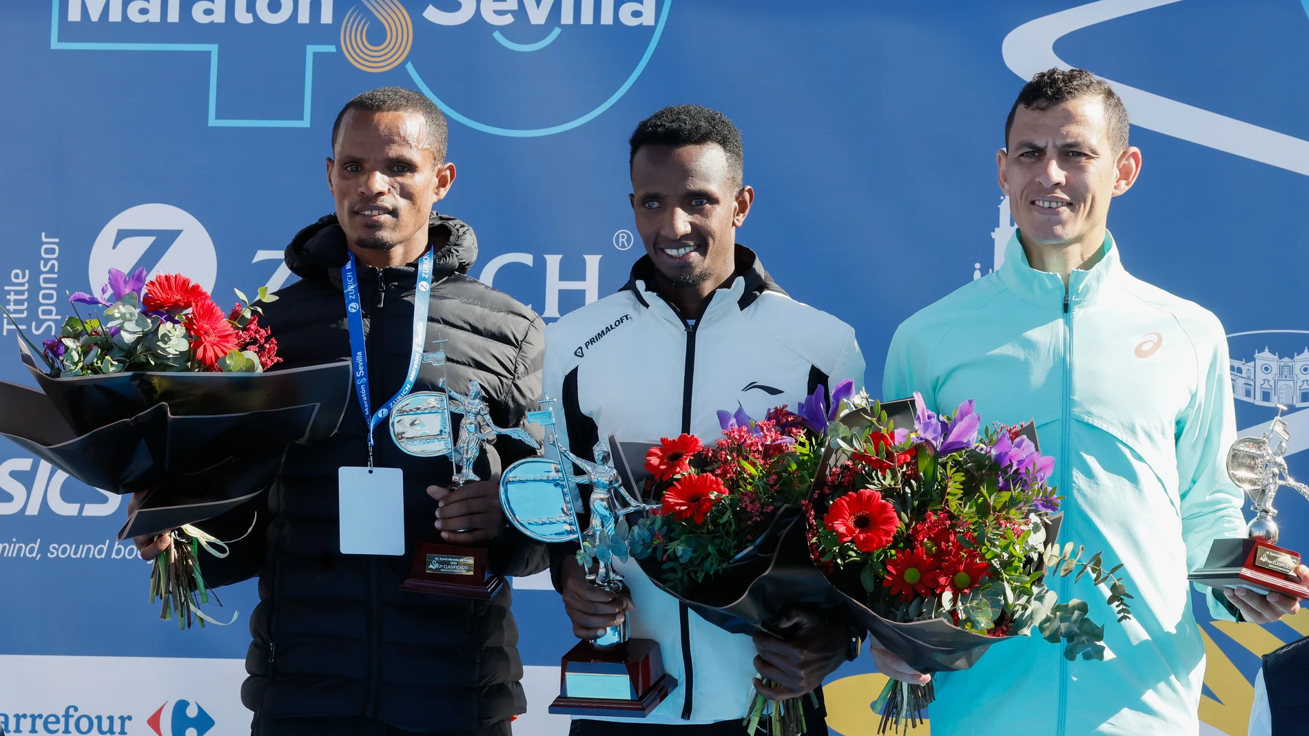 SEVILLA, 23/02/2025.- El atleta etíope Selemon Barega (c), oro, su compatriota Adisu Wegene (i), plata, y el marroquí Mohamed Reda El Aaraby (d), bronce, en el podio de la competición masculina en la cuadragésima edición del Maratón de Sevilla, este domingo en la capital andaluza. EFE/ José Manuel Vidal