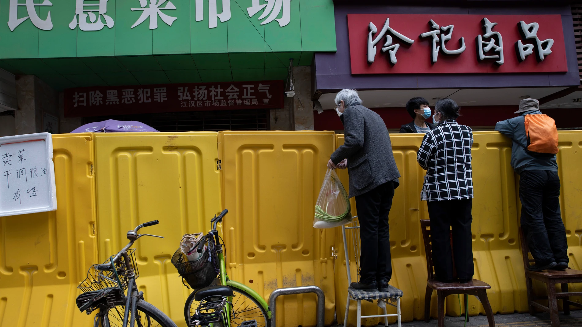 Residents climb onto chairs to buy groceries from vendors behind barriers used to seal off a neighborhood in Wuhan in central China's Hubei province on April 3, 2020. (AP Photo/Ng Han Guan)