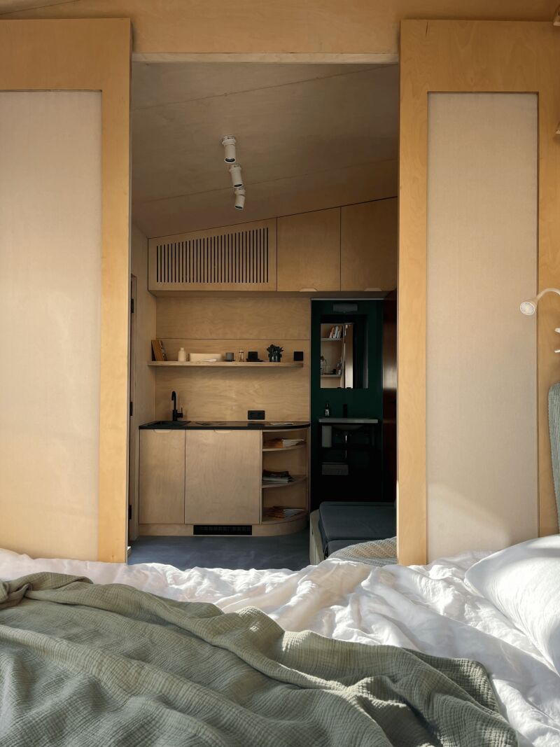 Una parte de la cama doble, el sofá, la cocina y el baño de fondo