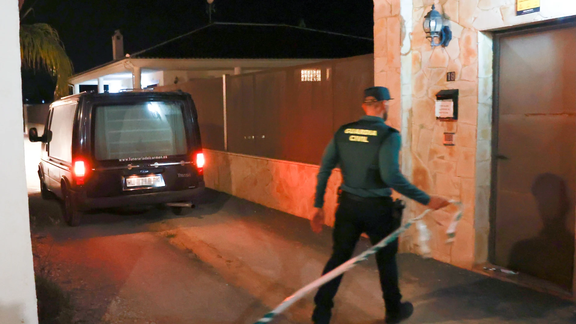 Un coche fúnebre y un agente de la Guardia Civil junto a la puerta donde tuvo lugar el suceso
