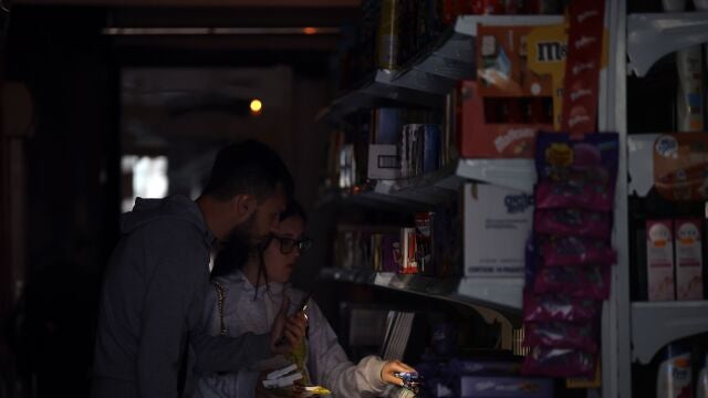 Varios clientes se iluminan con el móvil en un supermercado del centro de Barcelona durante el corte de suministro eléctrico que afecta este lunes a España y que ha dejado sin servicio el metro y el tranvia de Barcelona y todas las líneas de ferrocarril en Barcelona, y sin red de teléfonos móviles ni internet.