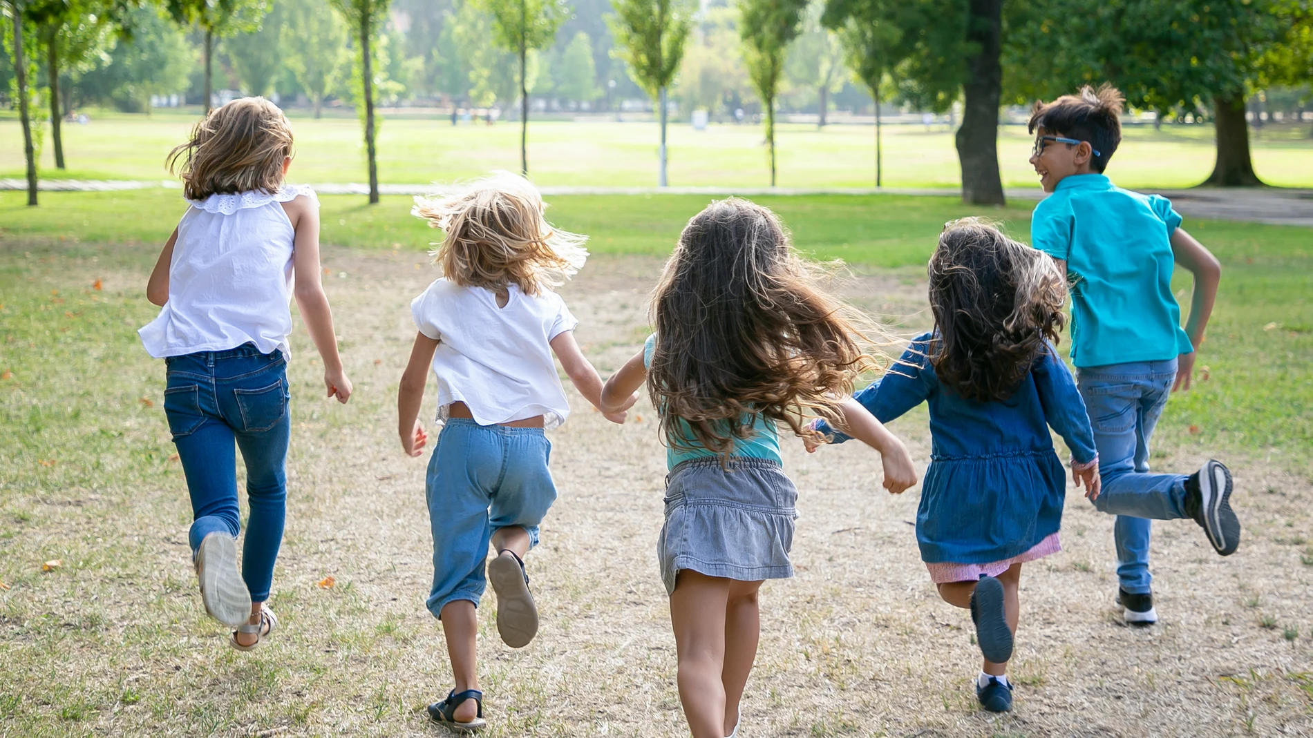 Grupo de niños corriendo juntos sobre la hierba, con carrera en el parque