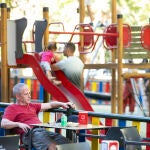 Un hombre toma algo en la terraza de un bar junto a parque infantil en Madrid.