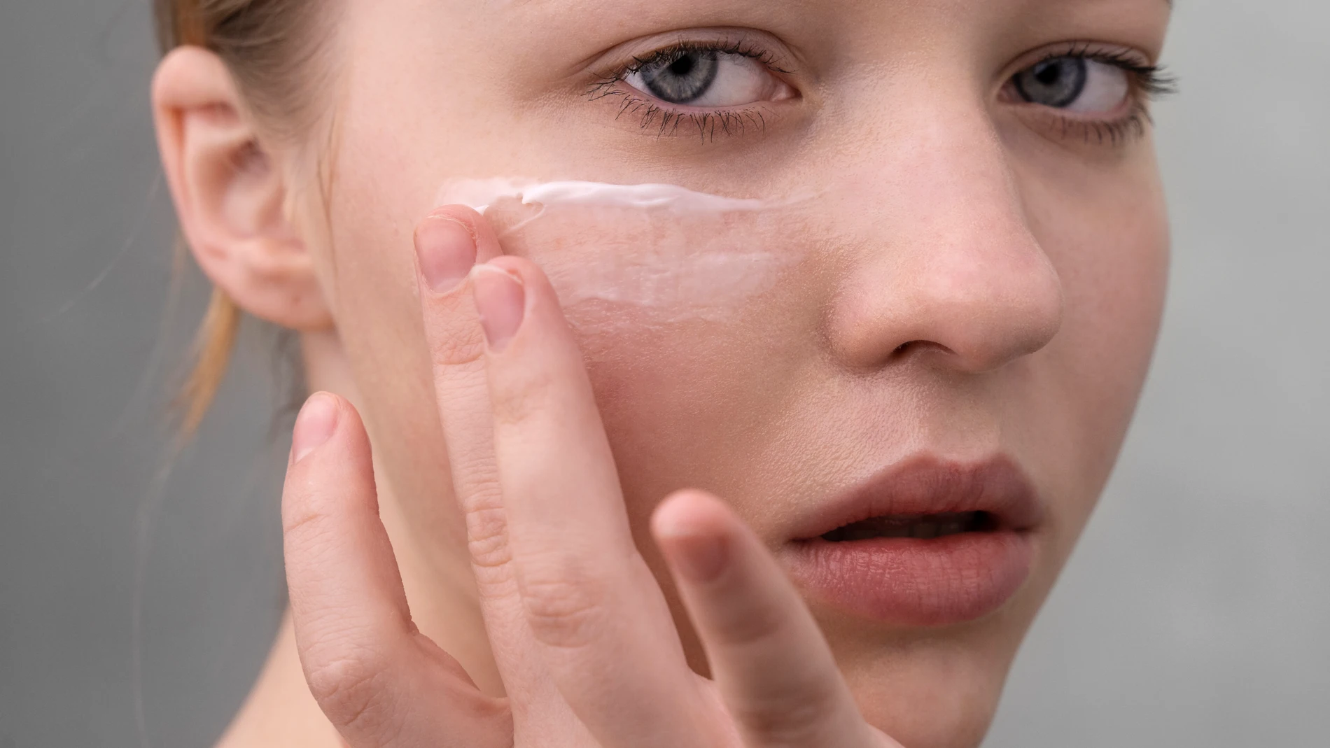 Mujer aplicando crema facial sobre la mejilla, detalle de rutina de cuidado de la piel.