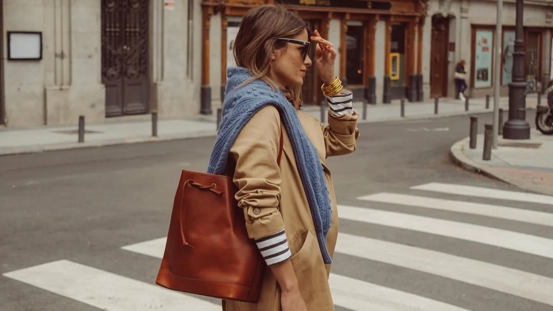 Influencer con gabardina beige, jersey de rayas marineras y bolso marrón, ejemplo de paleta de colores neutros para armario cápsula.