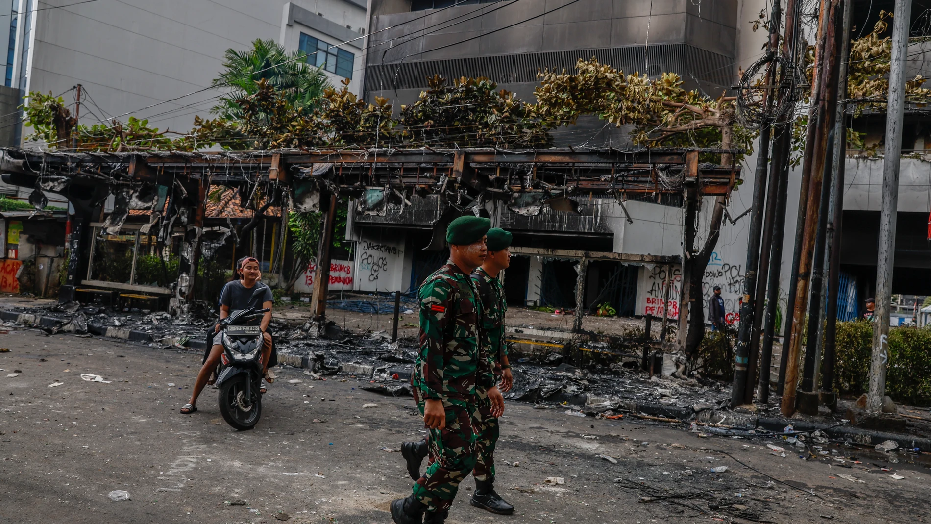 JAKARTA (Indonesia), 30/08/2025.- Military personnel walk past a burnt bus stop set on fire during a protest outside the Mobile Brigade police headquarter in Jakarta, Indonesia, 30 August 2025. Government buildings and police vehicles were set on fire during overnight protests across the country following the death of a motorbike hailing driver during an earlier protest against the housing allowance for members of parliament. (Protestas) EFE/EPA/MAST IRHAM