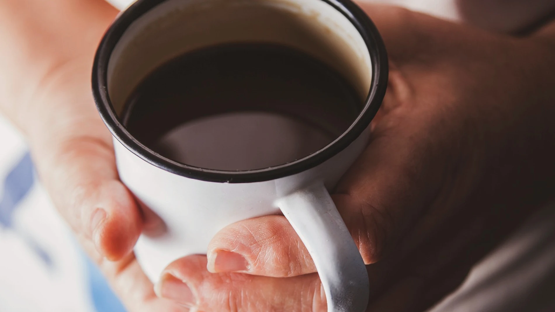 Taza de café caliente recién servido entre las manos de una persona