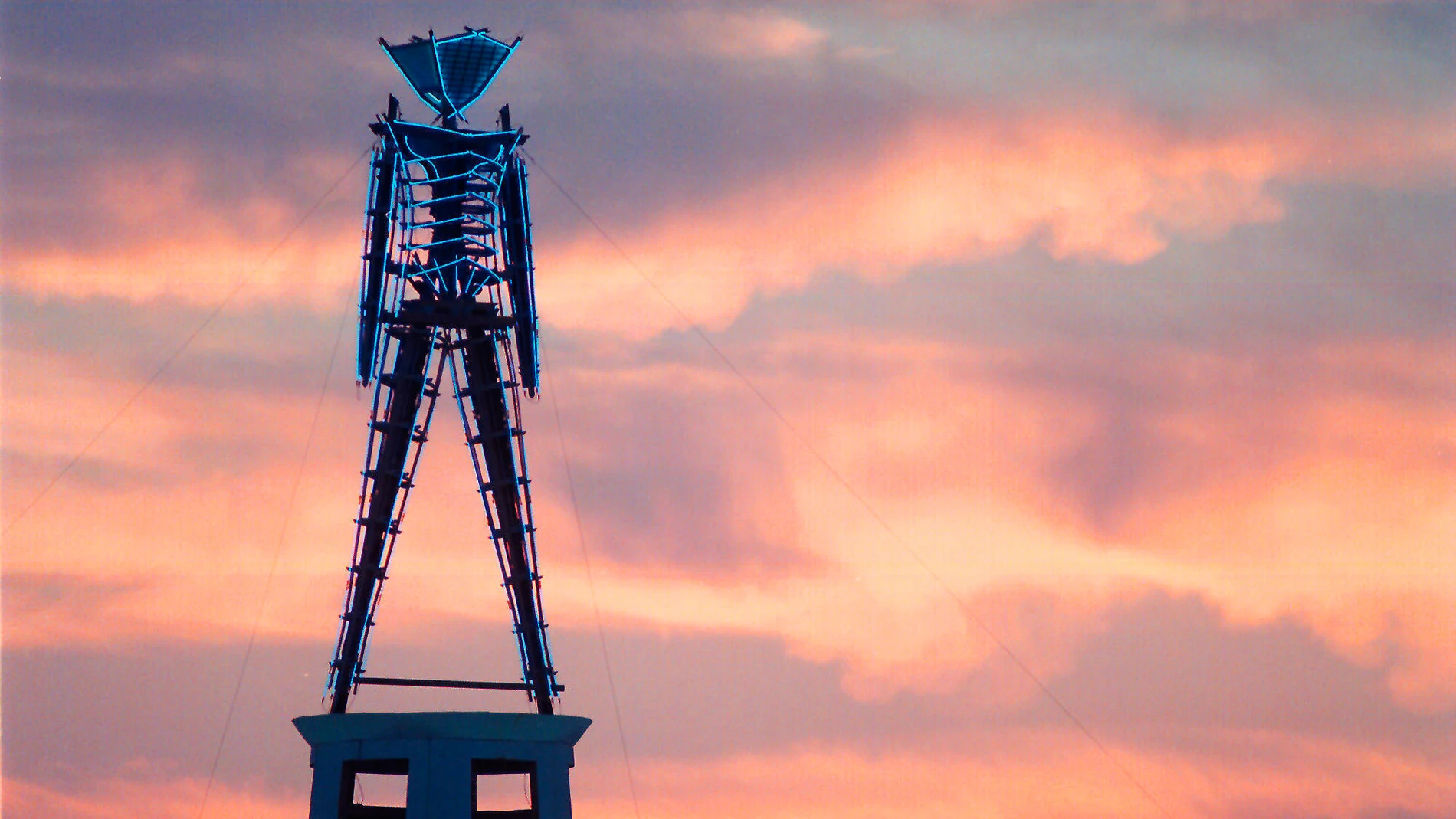 FILE - The sun rises behind a wood and neon statue, the center piece of the annual Burning Man festival north of Gerlach, Nev., Aug. 26, 2002. (AP Photo/Debra Reid, File)