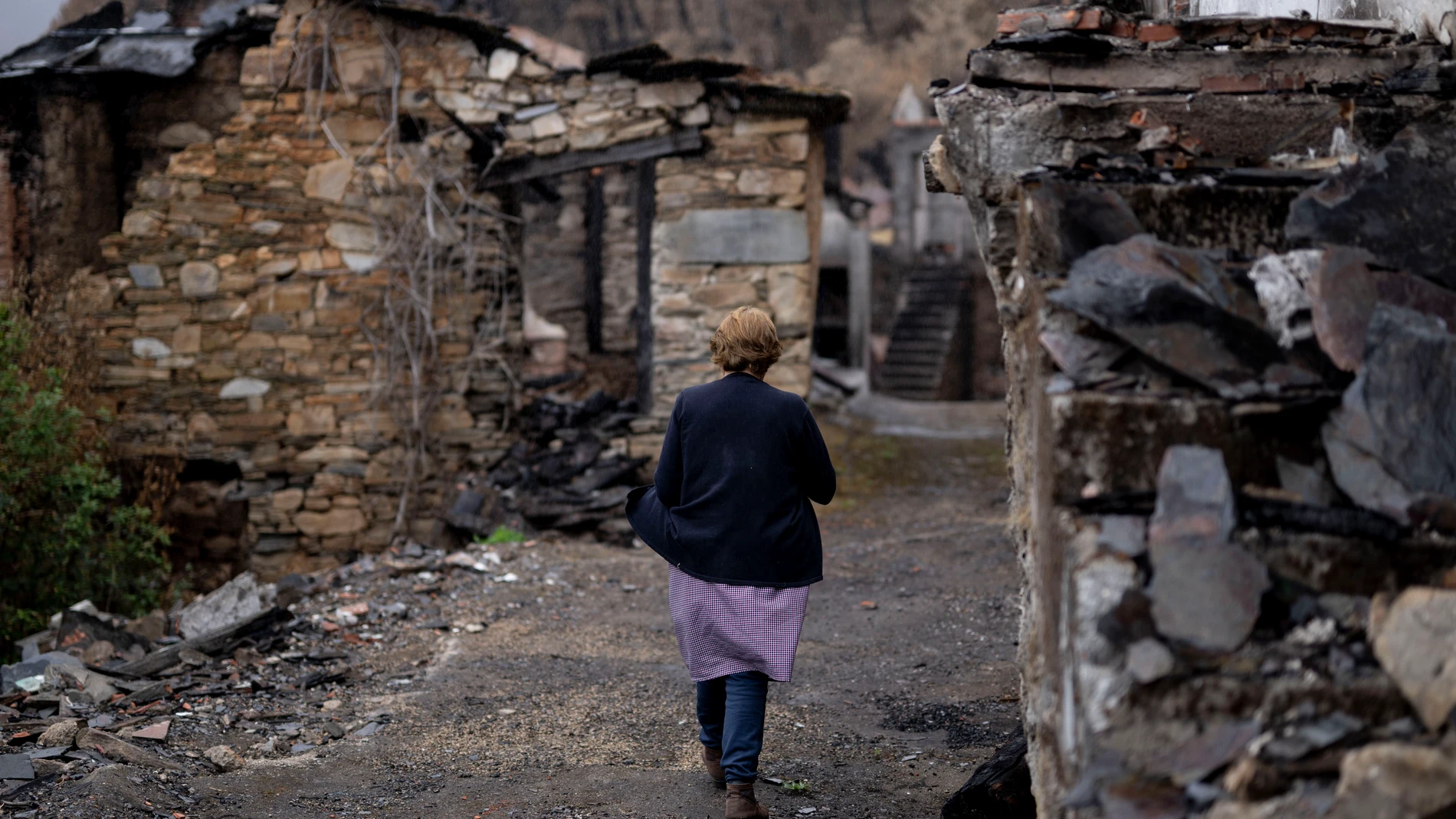 VILAMARTÍN DE VALDEORRAS (OURENSE) 12/09/2025.- Ana Sánchez camina entre las viviendas quemadas en San Vicente de Leira, en Vilamartín de Valdeorras (Ourense). Se cumple un mes del mayor incendio de la historia de Galicia, el que se originó en Larouco (Ourense) el pasado 13 de agosto y que calcinó más de 30.000 hectáreas. Los daños son aún visibles y los vecinos recuerdan con estupor lo sucedido mientras afrontan con desesperanza la reconstrucción. EFE/Brais Lorenzo