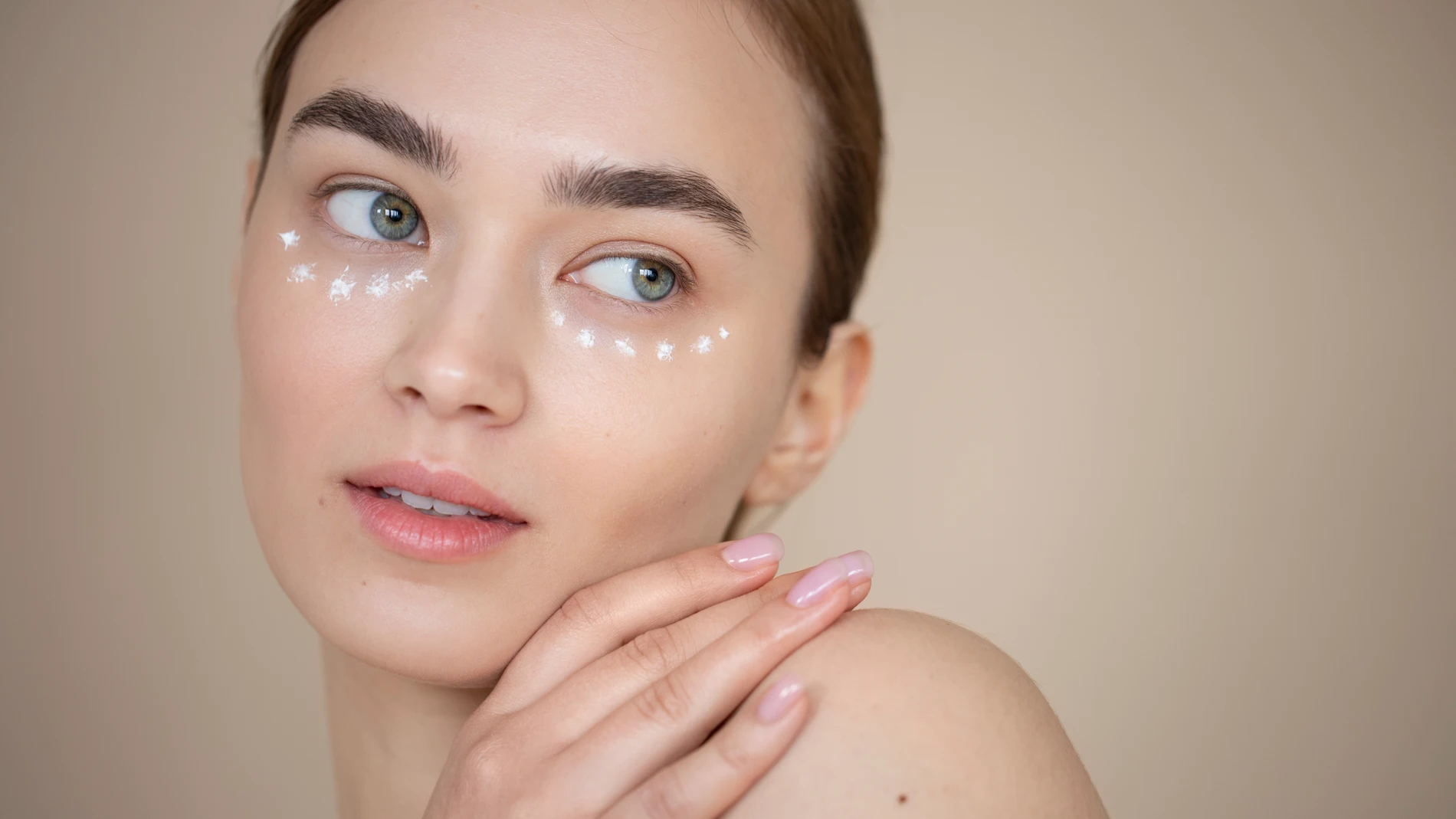 Mujer con crema en la zona inferior del contorno de ojos para preparar la piel antes del corrector.