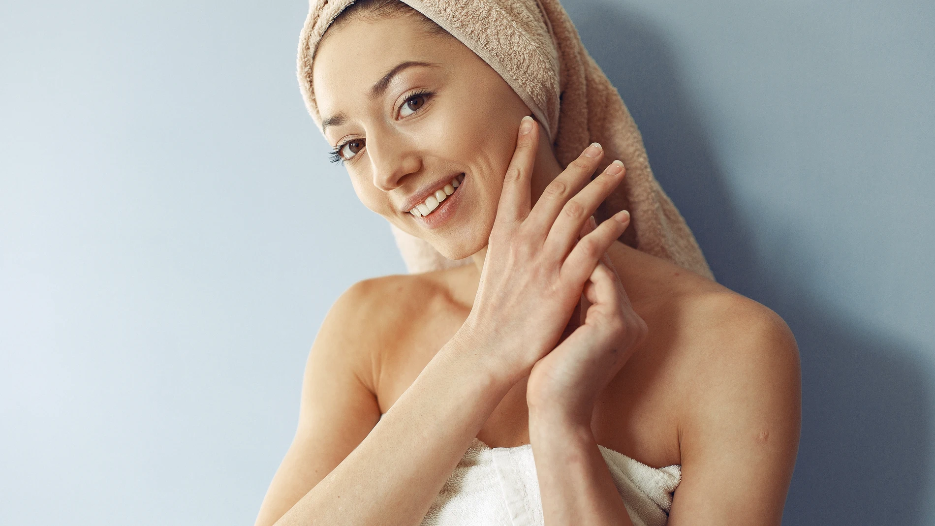 Mujer joven con toalla en la cabeza sonriendo después de su rutina de limpieza facial.