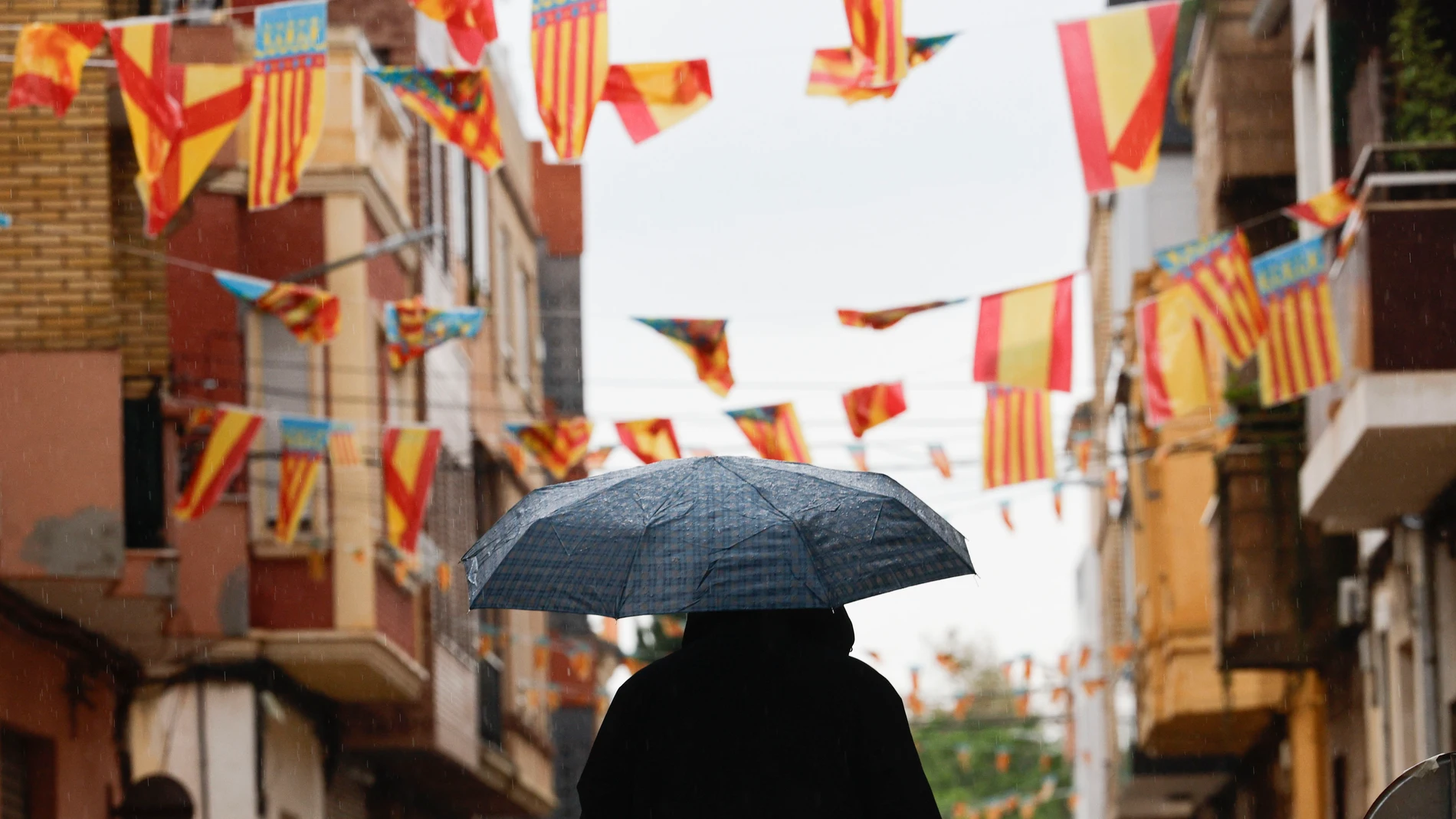 CATARROJA (VALÈNCIA), 09/10/2025.- Un hombre pasa con un paraguas bajo los banderines colgados en Catarroja (València), este 9 de octubre, Día de la Comunitat Valenciana.. El Centro de Coordinación de Emergencias de la Generalitat ha emitido un aviso especial ante la llegada de la dana Alice, con lluvias intensas y tormentas, que podrían dar lugar a inundaciones locales repentinas en zonas bajas, arroyos y ramblas, y que ha obligado a suspender los actos del Día de la Comunitat Valenciana. EF...