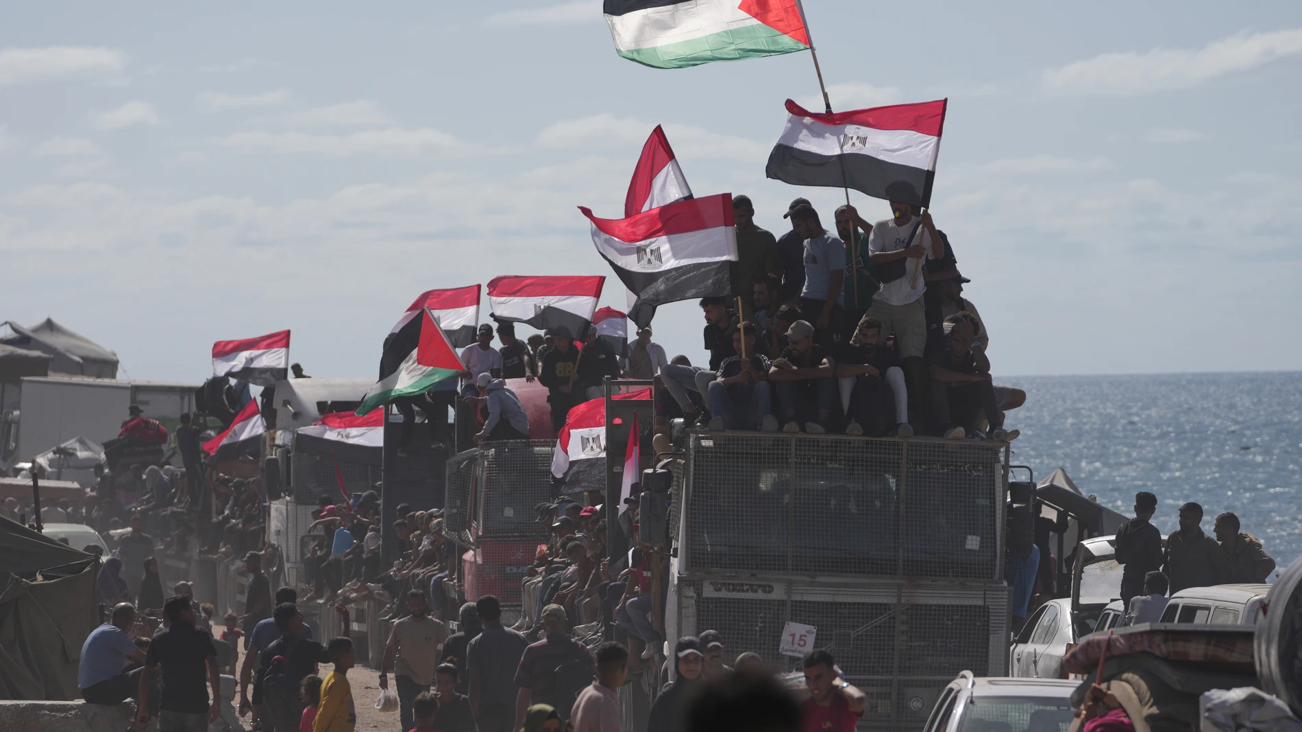 Displaced Palestinians ride on trucks loaded with belongings and wave Egyptian and Palestinian flags as they travel along the coastal road near Wadi Gaza in the central Gaza Strip, moving toward Gaza city, Saturday, Oct. 11, 2025, after Israel and Hamas agreed to a pause in their war and the release of the remaining hostages. (AP Photo/Jehad Alshrafi)