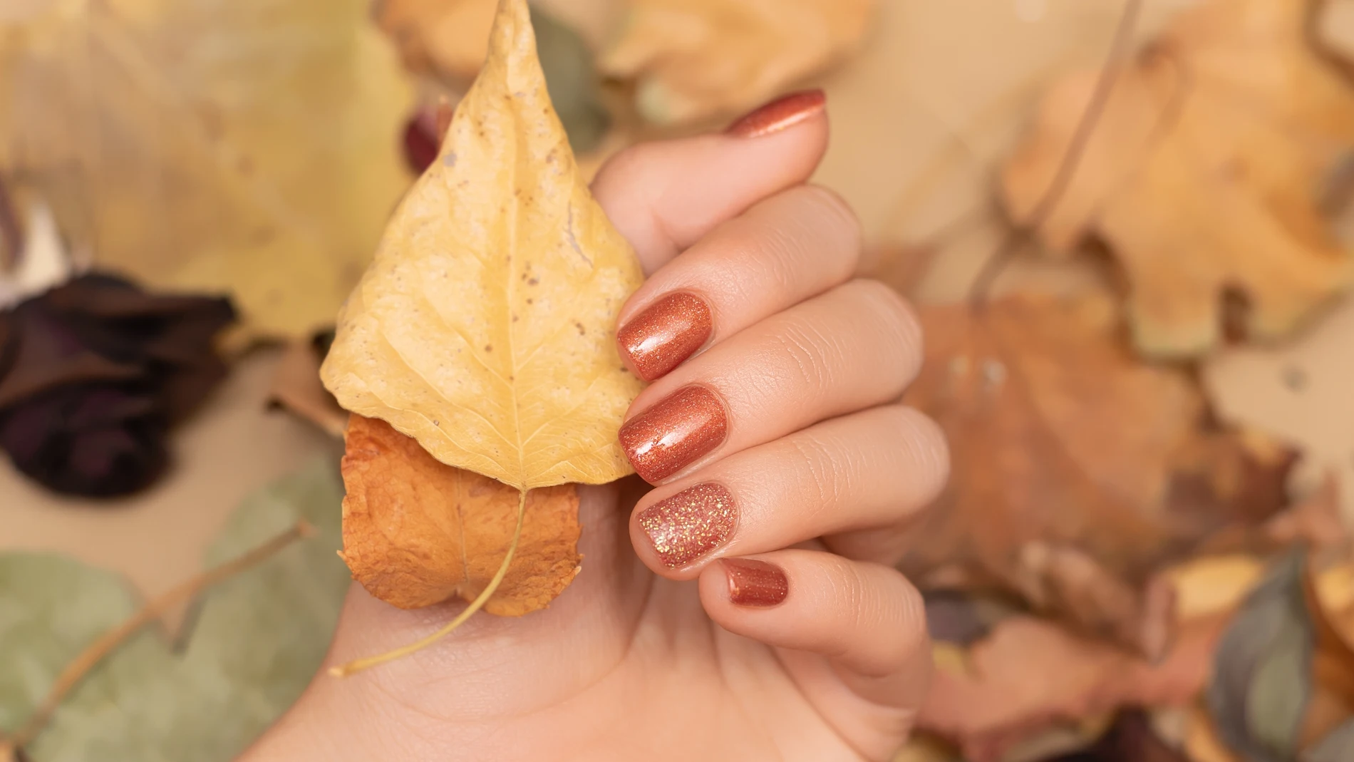 Mano de mujer sosteniendo hojas secas con manicura otoñal