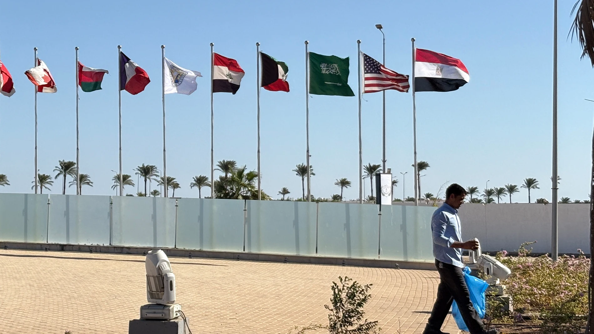 A worker walks past flags of participating countries at a summit hosted by the Egyptian government to celebrate the signing Israel-Hamas ceasefire deal at the Red Sea city of Sharm el-Sheikh, Egypt, Sunday, Oct. 12, 2025. (AP Photo)