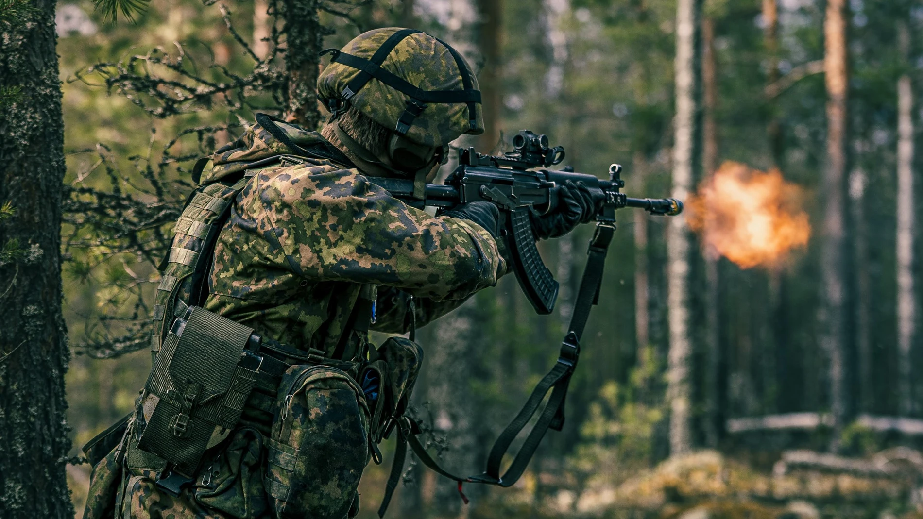 Soldado con camuflaje arbóreo disparando un fusil de asalto entre unos árboles