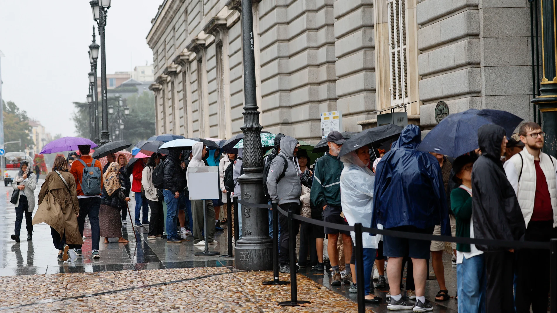 MADRID (ESPAÑA), 21/10/2025.- Los turistas se protegen de la lluvia a la entrada del Palacio Real este martes en Madrid. EFE/ Mariscal