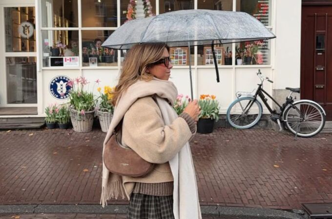 Influencer caminando bajo la lluvia con un paraguas transparente y un look otoñal en tonos beige.