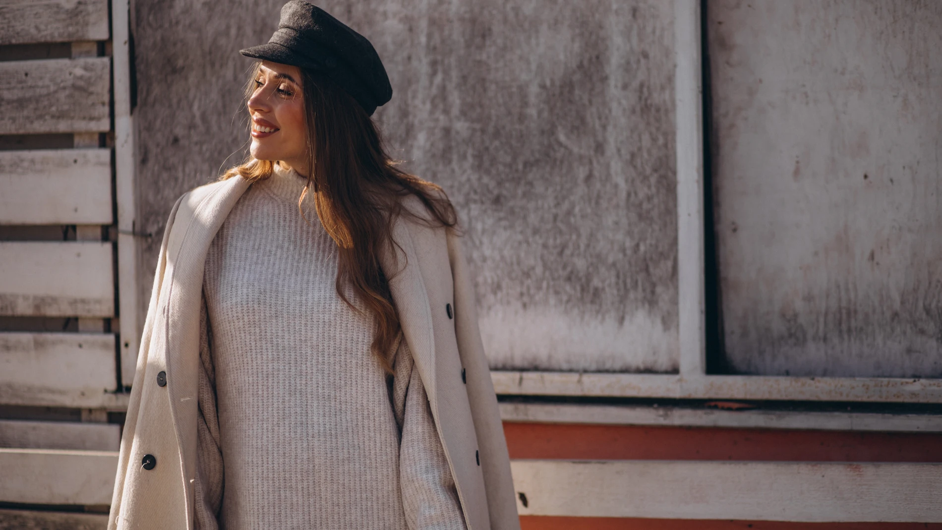 Mujer con vestido de punto y abrigo beige, sonriendo bajo el sol de otoño.
