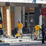 Vecinos limpian los destrozos causados ​​por un coche que se estrelló contra un negocio local, mientras la policía investiga el lugar de los hechos