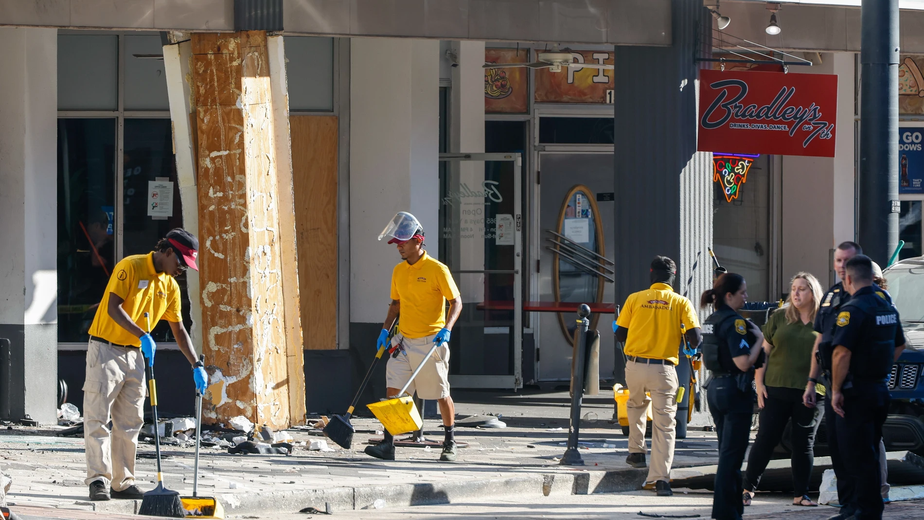 Vecinos limpian los destrozos causados por un coche que se estrelló contra un negocio local, mientras la policía investiga el lugar de los hechos