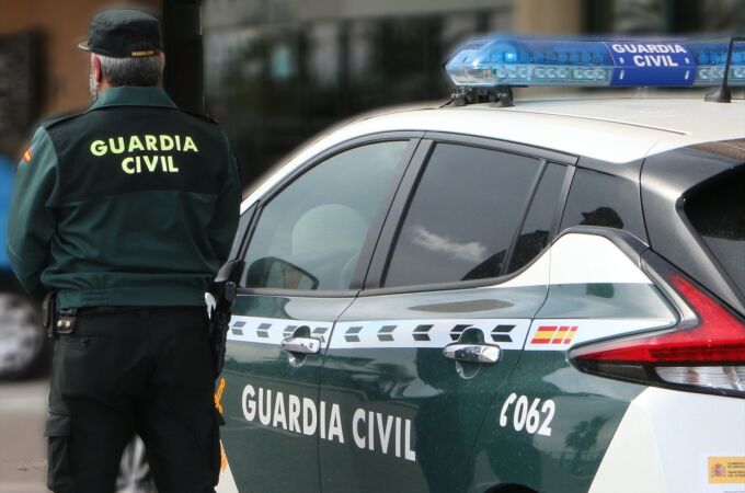Un agente de la Guardia Civil, de espaldas, de pie junto a un vehículo oficial.