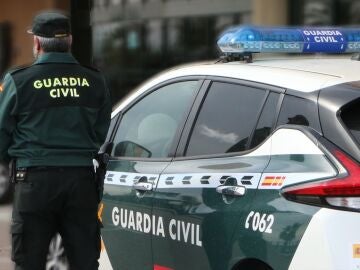 Un agente de la Guardia Civil, de espaldas, de pie junto a un vehículo oficial.