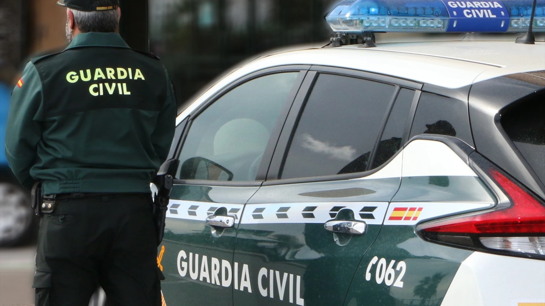 Un agente de la Guardia Civil, de espaldas, de pie junto a un vehículo oficial.