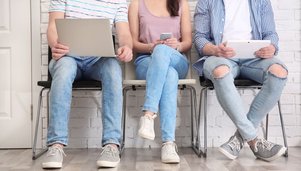 Tres j&oacute;venes con distintos dispositivos, port&aacute;til, m&oacute;vil y tablet