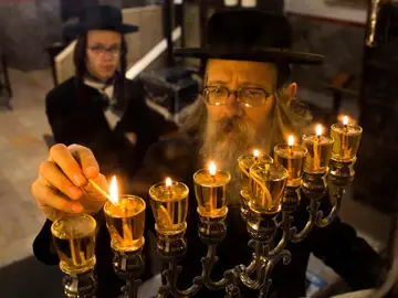 Hanukkah Explainer FILE - A Jewish ultra-Orthodox man lights candles during the last day of Jewish holiday of Hanukkah in Jerusalem's Mea Shearim neighborhood, Wednesday, Dec. 4, 2013. (AP Photo/Bernat Armangue, File)