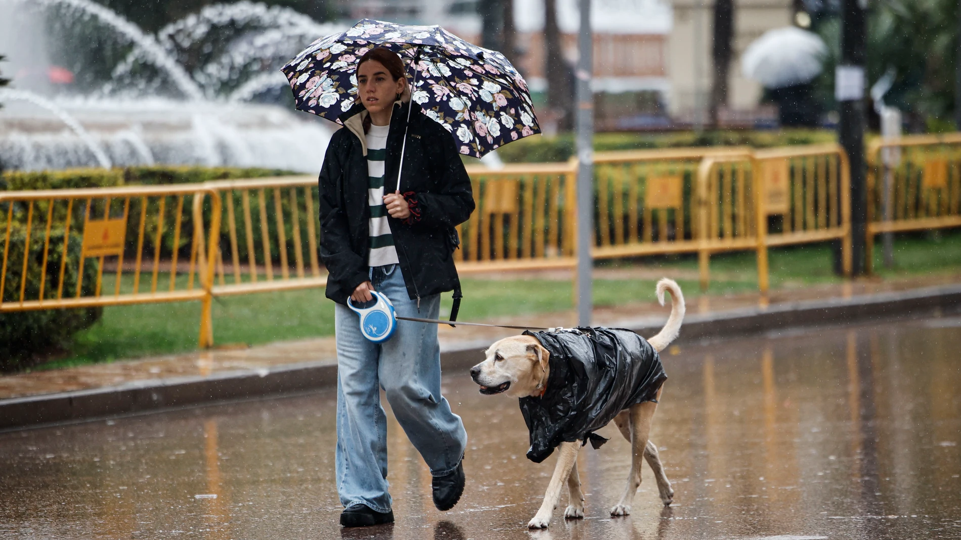 GRAFCVA1265. VALÈNCIA, 16/12/2025.- La Aemet ha establecido para este martes y miércoles el aviso amarillo por precipitaciones de hasta 30 litros por metro cuadrado en una hora, y 80 en doce horas, acompañadas de tormentas, en distintos puntos de la Comunitat Valenciana. En la imagen una joven pasea con su perro por la plaza del Ayuntamiento de València. EFE/Biel Aliño